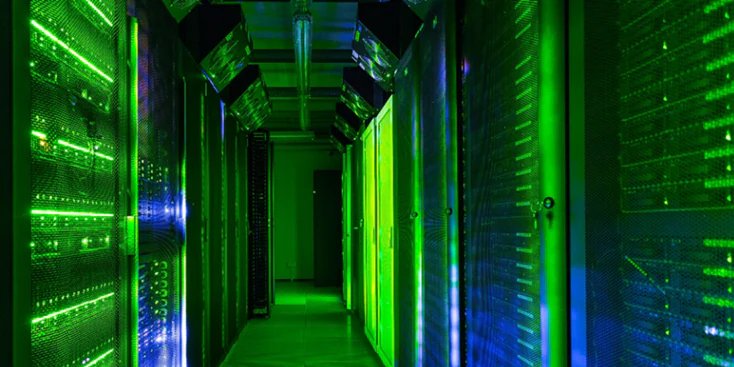 A brightly lit corridor in a modern data center features rows of server racks glowing with green and blue LED lights. The environment is highly controlled, with visible ventilation and cable management overhead.