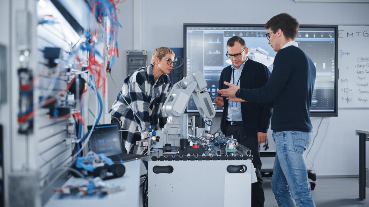 A group of engineers is gathered around a robotic arm in a modern laboratory setting