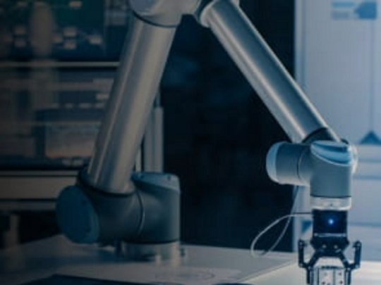 A robotic arm is actively engaged in a laboratory or manufacturing environment, manipulating objects on a work surface.