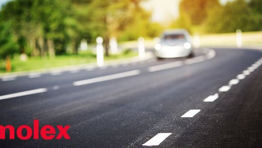 Route asphaltée incurvée avec des marquages blancs, une voiture floue au loin, et le logo de l'entreprise "molex" en bas.