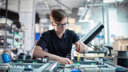 Technician working on electronic components and wiring in a manufacturing facility.