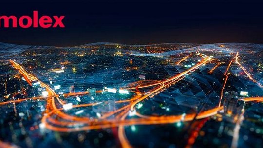 A vibrant cityscape at night featuring illuminated roads and buildings, with the Molex logo prominently displayed in the upper left corner. The image showcases a futuristic network concept with glowing pathways and geometric overlays. The scene conveys innovation and connectivity in an urban setting.