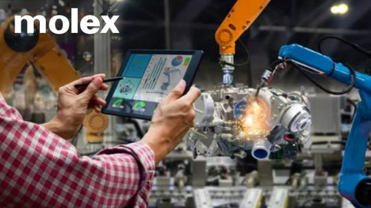 A factory setting showcasing advanced robotic arms assembling machinery parts. A person in a plaid shirt uses a tablet displaying data and analytics to monitor the process. The Molex logo is clearly visible, emphasizing the brand's involvement in industrial automation.