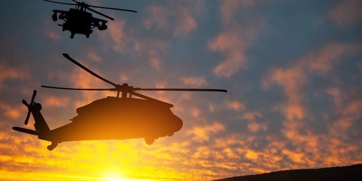 Two helicopters are silhouetted against a vibrant sunset sky, creating a dramatic and dynamic scene. 