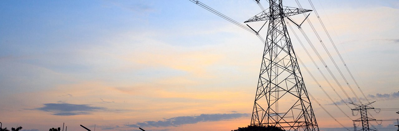 A tall metal power transmission tower stands prominently against a colorful sunset sky. 