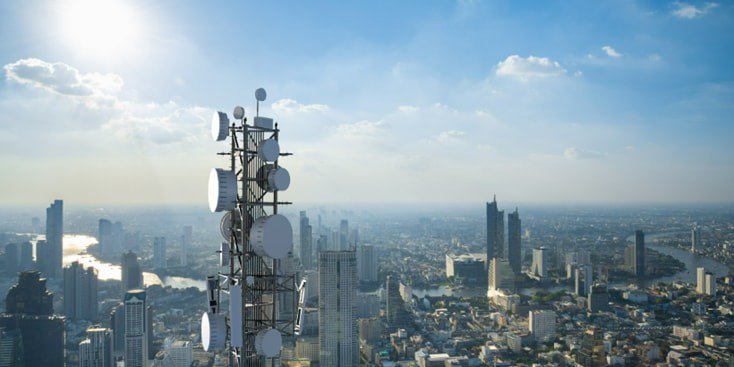 A telecommunication tower equipped with multiple antennas stands prominently against a sprawling cityscape. 