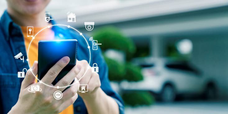 A close-up of a person holding a smartphone, interacting with smart home icons displayed digitally around the device.