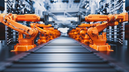 La imagen presenta múltiples brazos robóticos de color naranja brillante operando a lo largo de una cinta transportadora en un entorno industrial de alta tecnología.