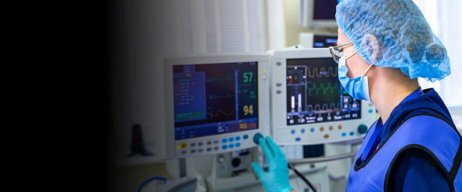 Medical professional operating patient monitoring equipment with multiple screens displaying vital signs in a clinical setting.