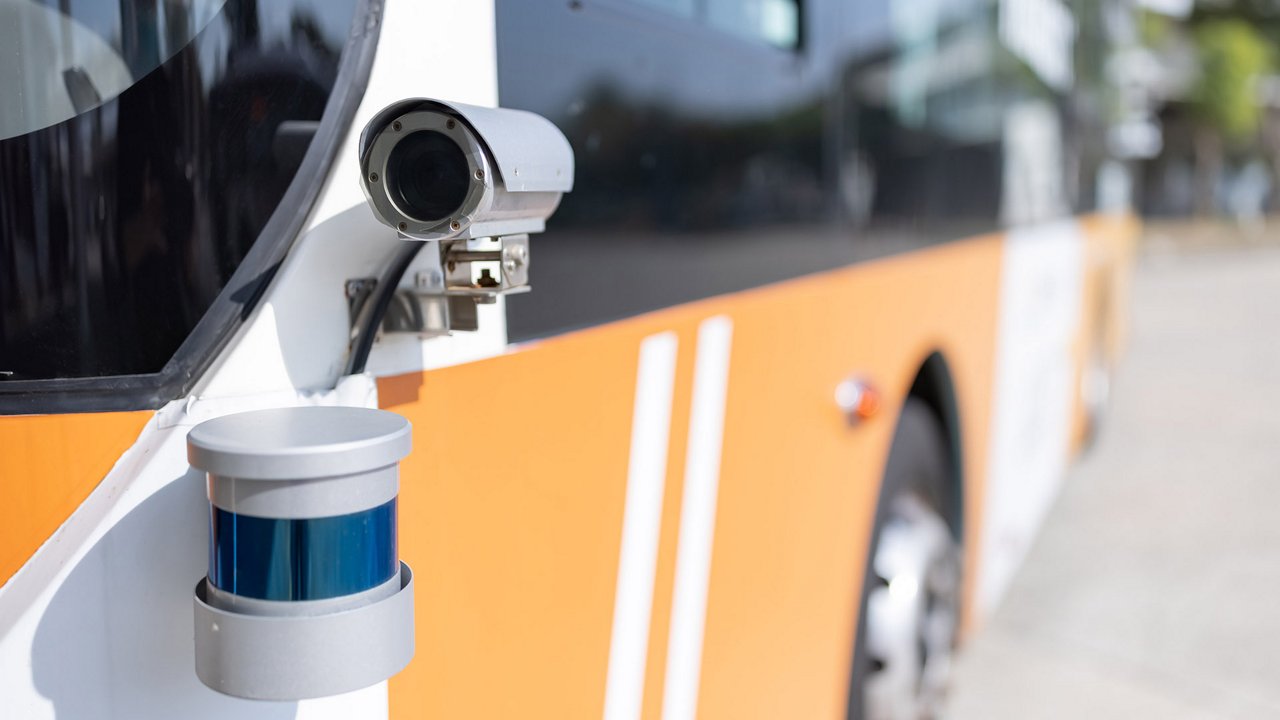 Close-up of a surveillance camera mounted on the exterior of an orange and white public bus.