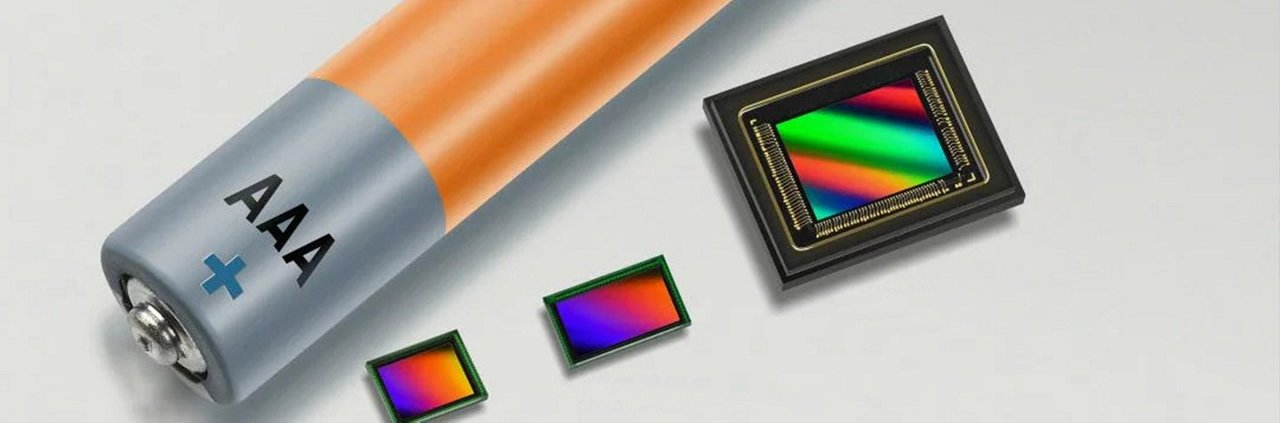 Close-up of an AAA battery placed next to three colorful microchips on a light surface. 