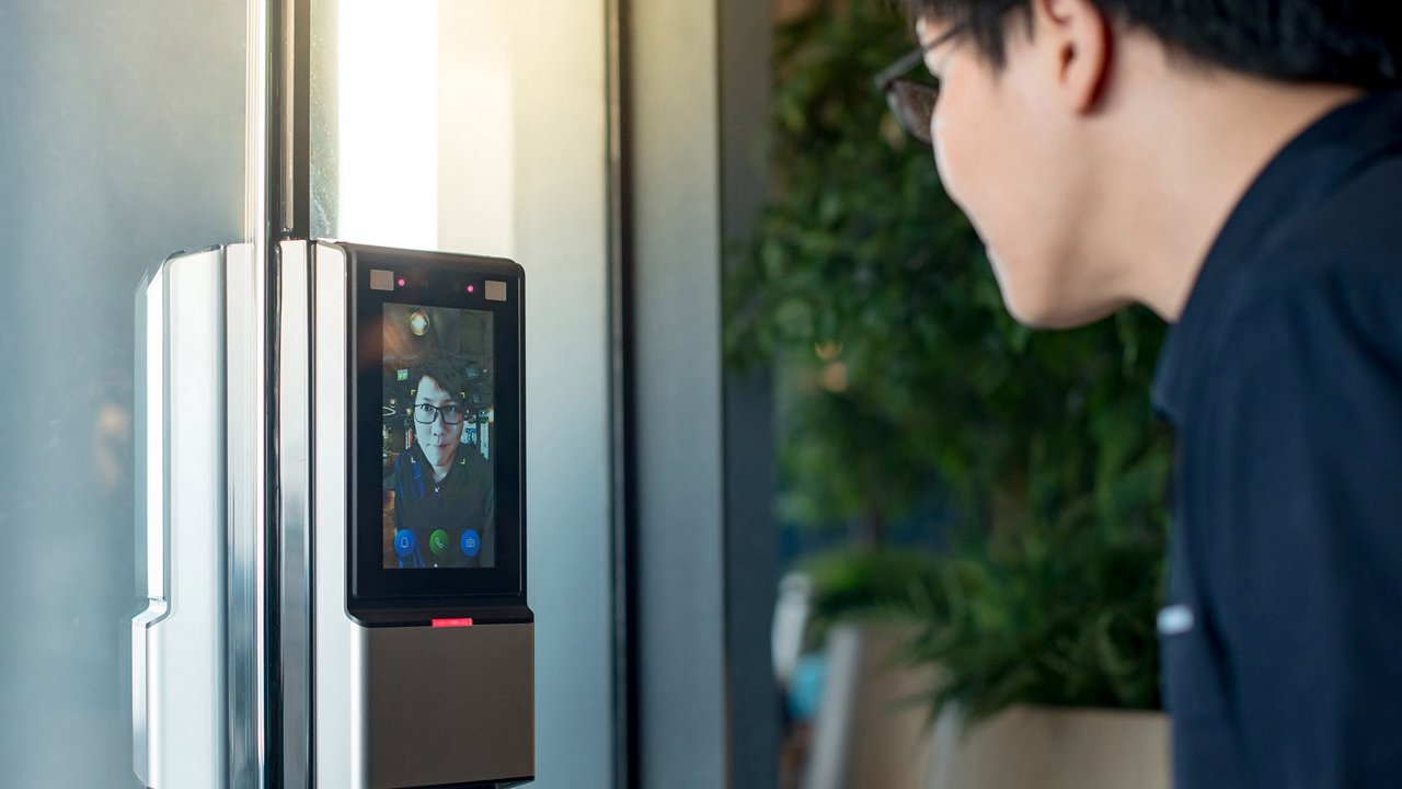 A sleek facial recognition device is mounted on a glass door in a contemporary indoor environment.