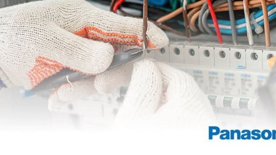 A close-up of a technician's gloved hands working on an electrical panel with various wires and switches. 