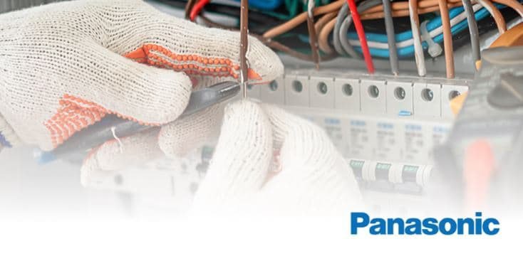 A close-up of a technician's gloved hands working on an electrical panel with various wires and switches. 