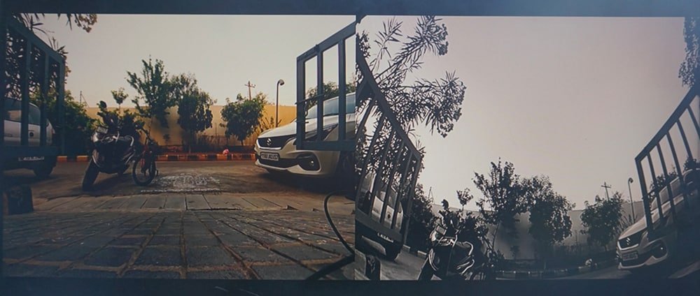 A parking area featuring a motorcycle and a car, surrounded by trees and a gated entrance