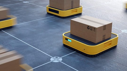 노란색 로봇 플랫폼이 격자 무늬가 있는 창고 바닥을 따라 상자들을 운반합니다.