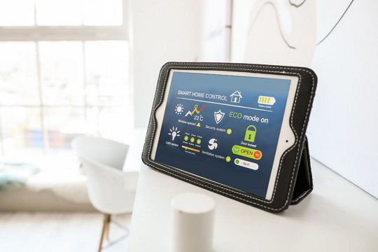 A tablet displaying smart home control features is placed on a white surface in a bright, modern room.