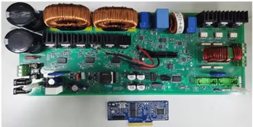 A detailed image of a green electronic circuit board featuring various components such as capacitors, coils, heat sinks, and connectors. The board is laid out on a white surface, with a smaller blue circuit board positioned below it.