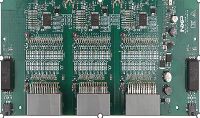 This image shows a detailed view of a green printed circuit board featuring multiple integrated circuits, capacitors, and connectors. The board is densely populated with electronic components arranged in a symmetrical pattern. Three large connectors are visible at the bottom, with various resistors and chips distributed across the surface.