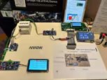 A tabletop setup features an electronic demonstration board with multiple connected sensor modules and digital screens.