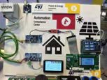 A demonstration board showcases a smart home automation system with various electronic components and display screens. The setup includes visible wiring, circuit boards, and a central touchscreen interface.