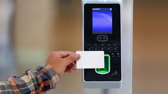 A person holds a white access card up to an electronic security reader. 