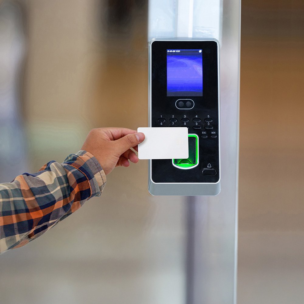 A person holds a white access card up to an electronic security reader. 