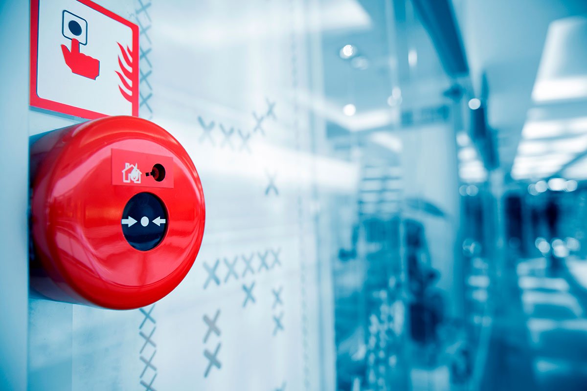A bright red fire alarm button is mounted on a glass wall in a modern building corridor. 