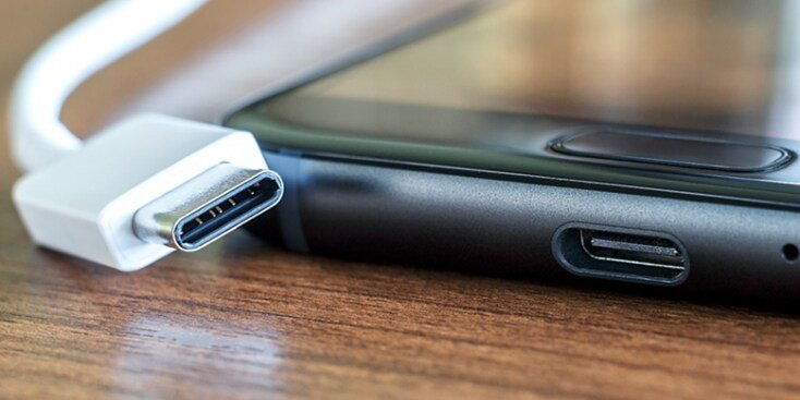 A detailed view of a USB-C cable connector positioned next to a smartphone's USB-C port. The setup is placed on a wooden surface, emphasizing the modern design and functionality of the device. The image highlights connectivity and technology essentials.