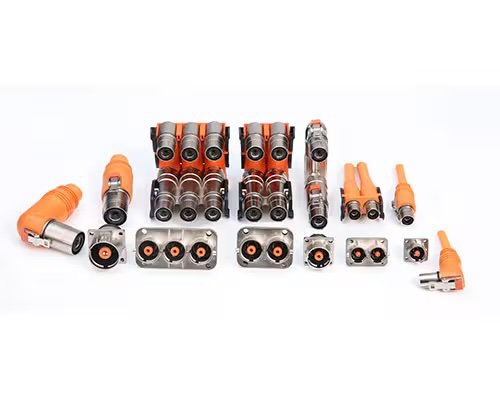 A collection of various industrial electrical connectors is arranged in rows on a white background. The connectors are predominantly orange and metallic, featuring different shapes and pin configurations.