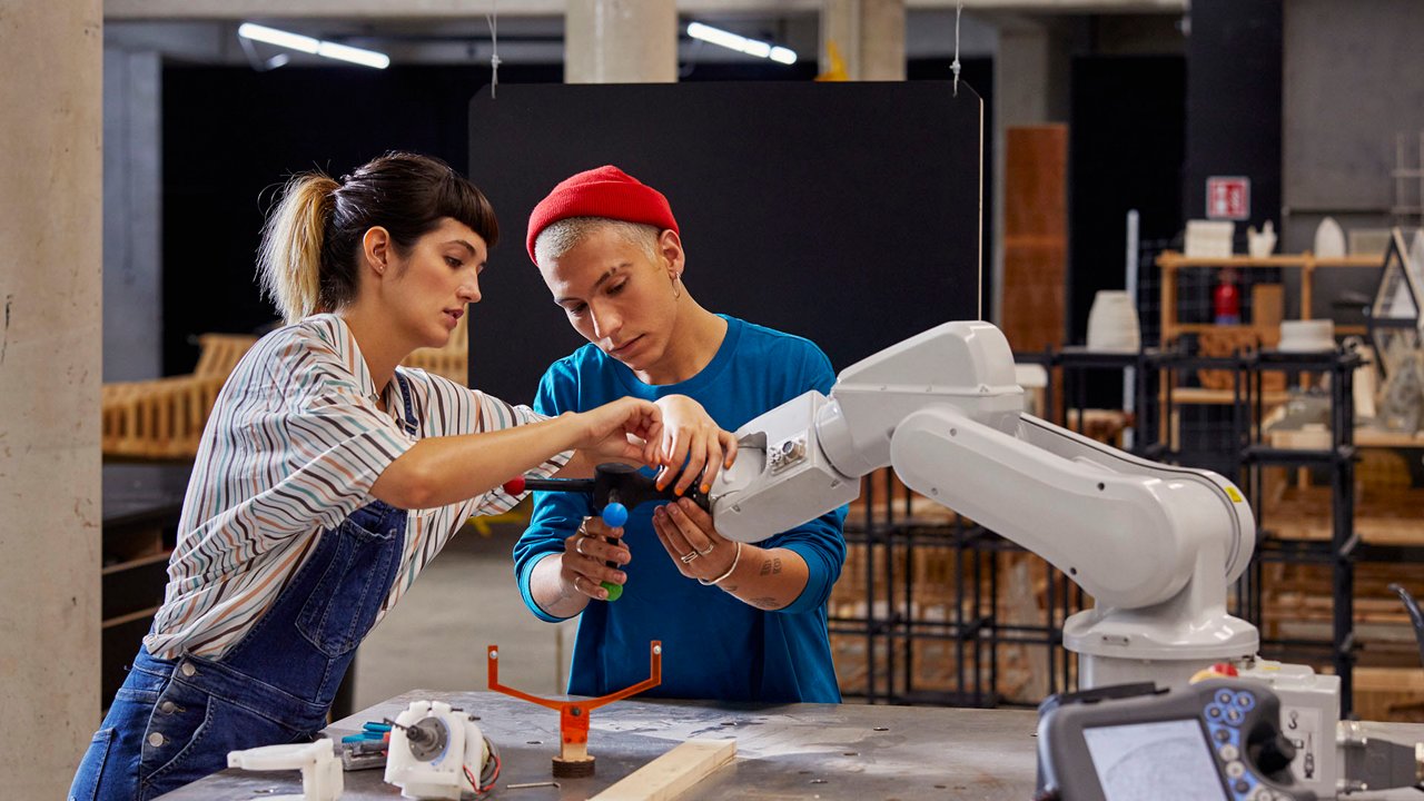 두 사람이 산업 환경에서 로봇 팔과 함께 작업합니다.