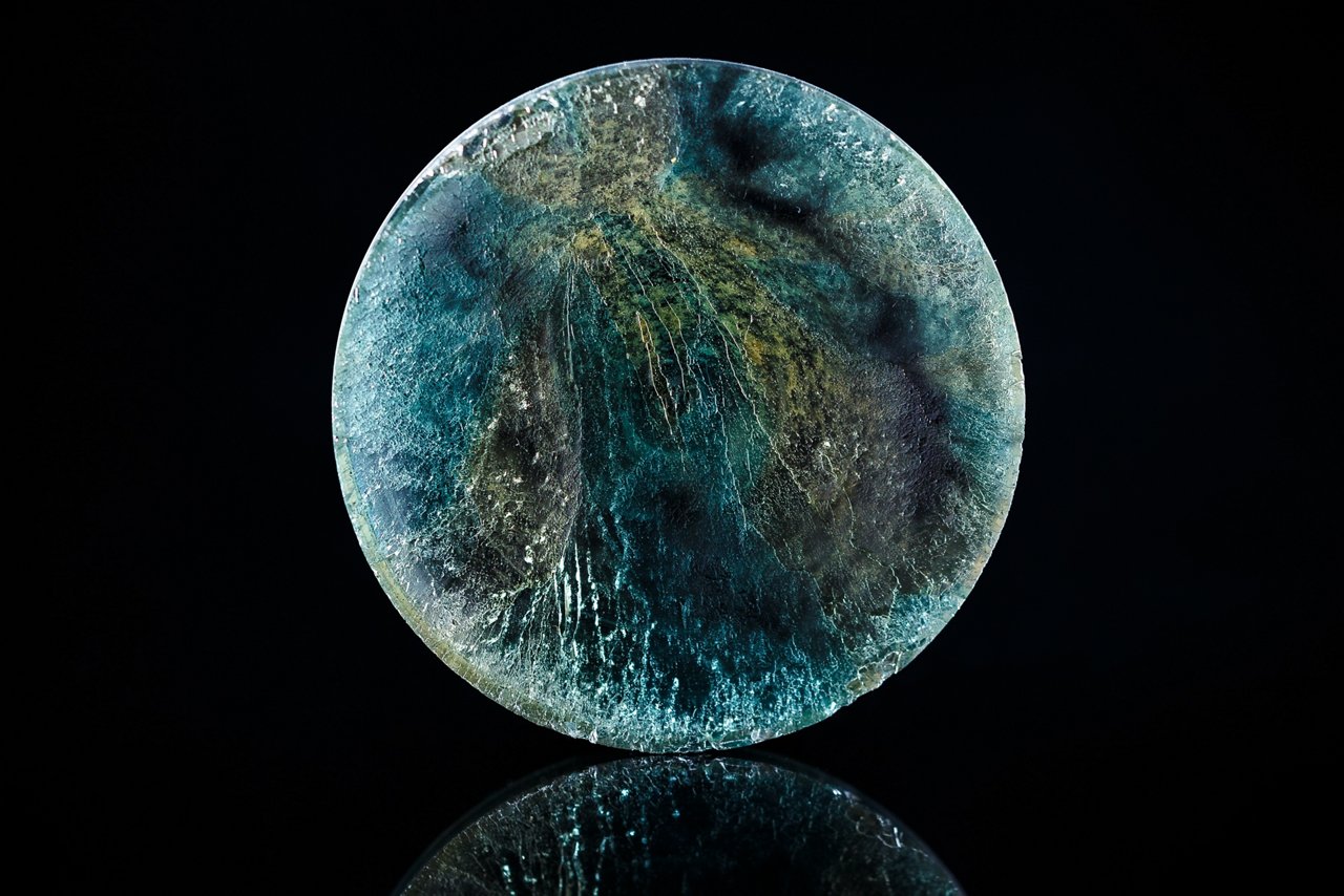 The main subject is a round, abstract object featuring swirling patterns in blue, green, and hints of yellow.