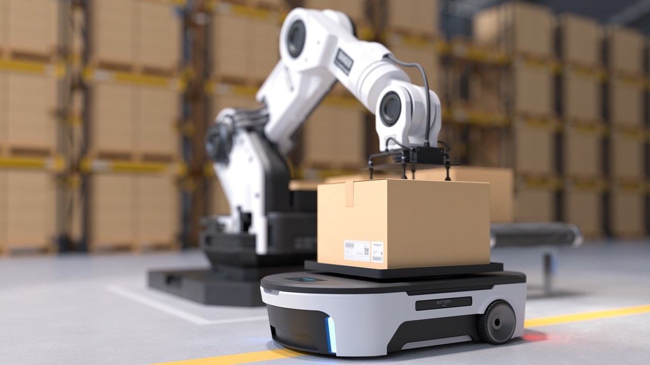 A robotic arm carefully places a cardboard box onto a small autonomous mobile cart in a warehouse environment. 
