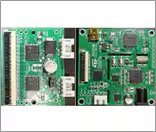 This image shows two green printed circuit boards side by side, each populated with various electronic components such as integrated circuits, capacitors, and connectors. The boards feature visible traces, chips, and ports, with some white text and numbers printed on the surface.