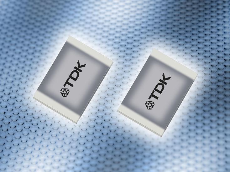 Two TDK electronic components are displayed on a textured, metallic surface.