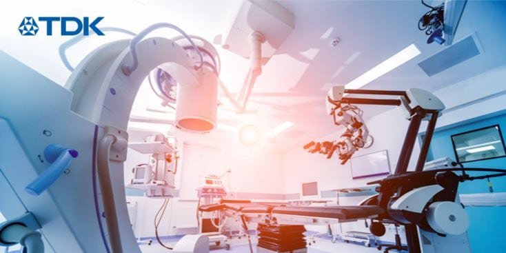 Une installation médicale de haute technologie équipée d'appareils de diagnostic et chirurgicaux avancés. Le cadre est une salle d'hôpital stérile et bien éclairée avec des bras robotiques et des dispositifs d'imagerie. Le logo TDK est clairement visible dans le coin supérieur gauche, mettant en avant la marque. La scène met en évidence la technologie de pointe dans le domaine de la santé.