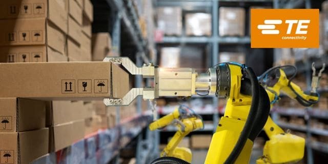 Un braccio robotico viene visto sollevare una scatola di cartone in un magazzino, dimostrando l'automazione nella logistica.