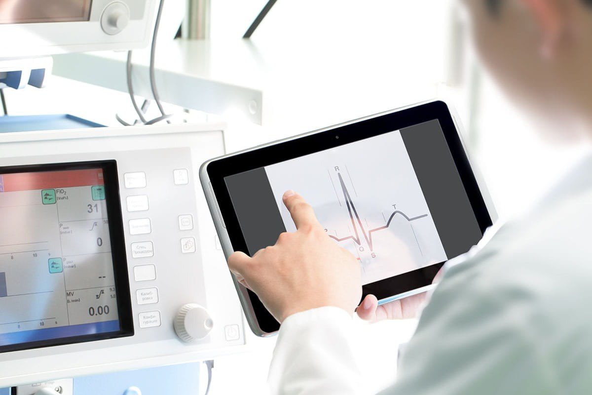 A medical professional interacts with a tablet displaying heart rate data in a clinical setting