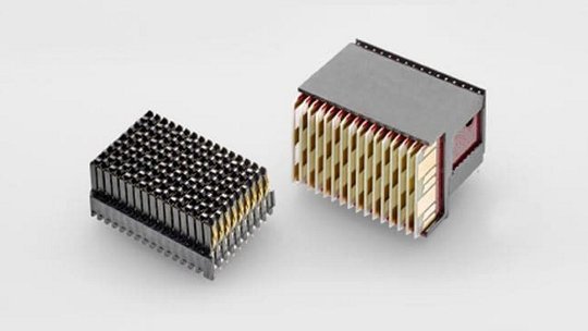 Two compact electronic heat sinks are displayed against a neutral gray background. The designs feature metallic fins arranged vertically and horizontally for efficient heat dissipation. The left unit has a darker finish, while the right unit showcases a combination of silver and gold tones. These components are essential for thermal management in electronic devices.