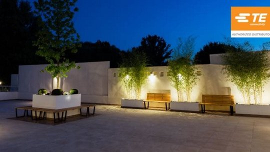 A contemporary outdoor patio featuring minimalist benches and planters illuminated by warm evening lights.