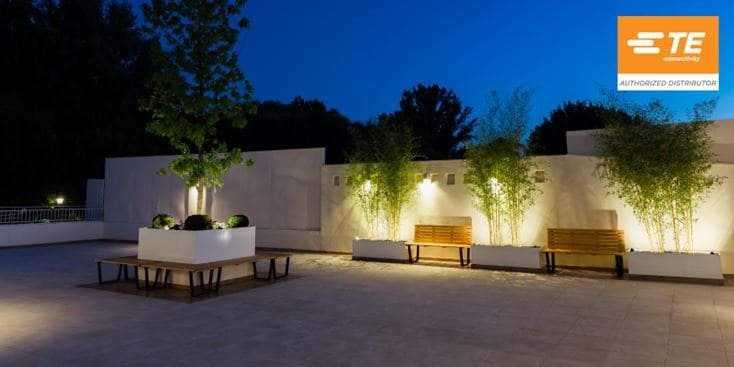 Un patio esterno contemporaneo con panche e fioriere minimaliste illuminate da calde luci serali.