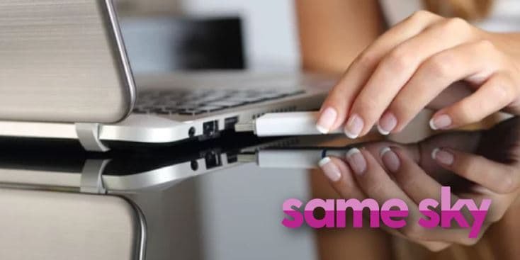 A close-up of a hand inserting a USB device into the port of a sleek silver laptop