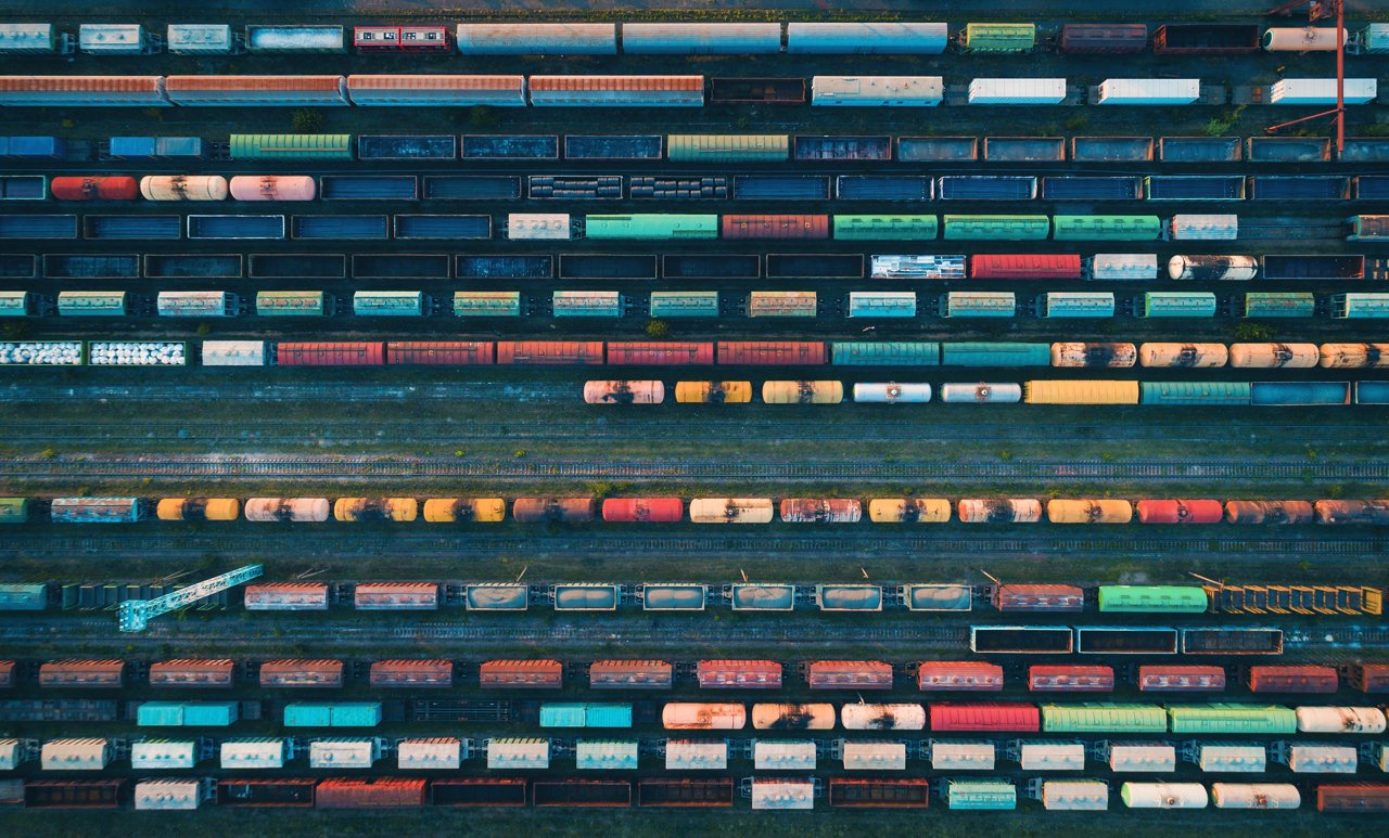 An overhead view of a large rail yard with many colorful freight train cars arranged on multiple parallel tracks.
