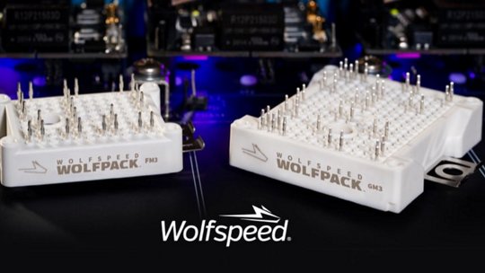 Two Wolfspeed Wolfpack power modules, PKM and GM2, are displayed in a high-tech environment with illuminated components in the background.
