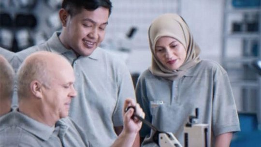 A group of individuals wearing gray uniforms is gathered around a piece of industrial equipment in a professional setting