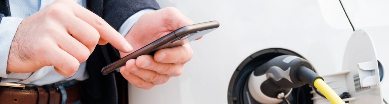 Un hombre usando un teléfono inteligente para pagar; Coche eléctrico (EV) cargando en una estación