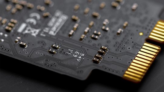 详细视图展示了一块黑色电子电路板，配有镀金连接器。该电路板展现了复杂的组件和焊接细节，突出了精密工程的特点。可见的文字包括“12V”和其他技术标记，突显其电气规格。