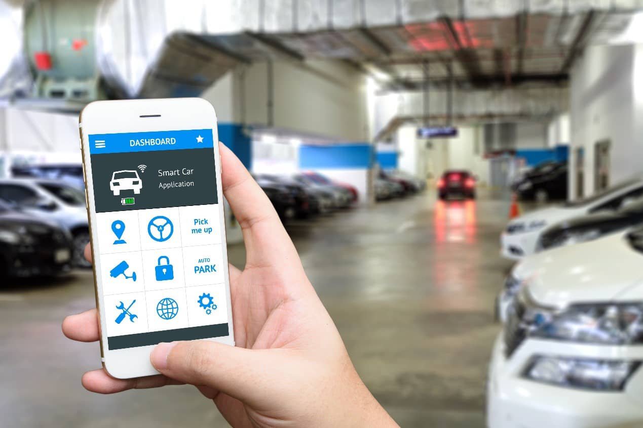 Image of hand holding smart phone and application dashboard with blur car parking garage