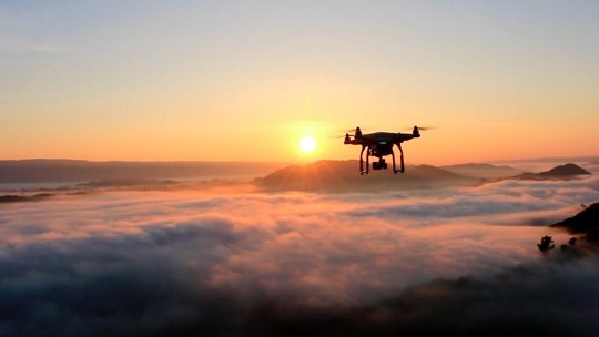 Image of drone flying above clouds at sunrise