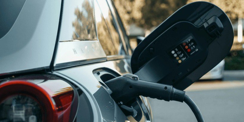 Acercamiento de un vehículo eléctrico conectado a una estación de carga en un entorno exterior.